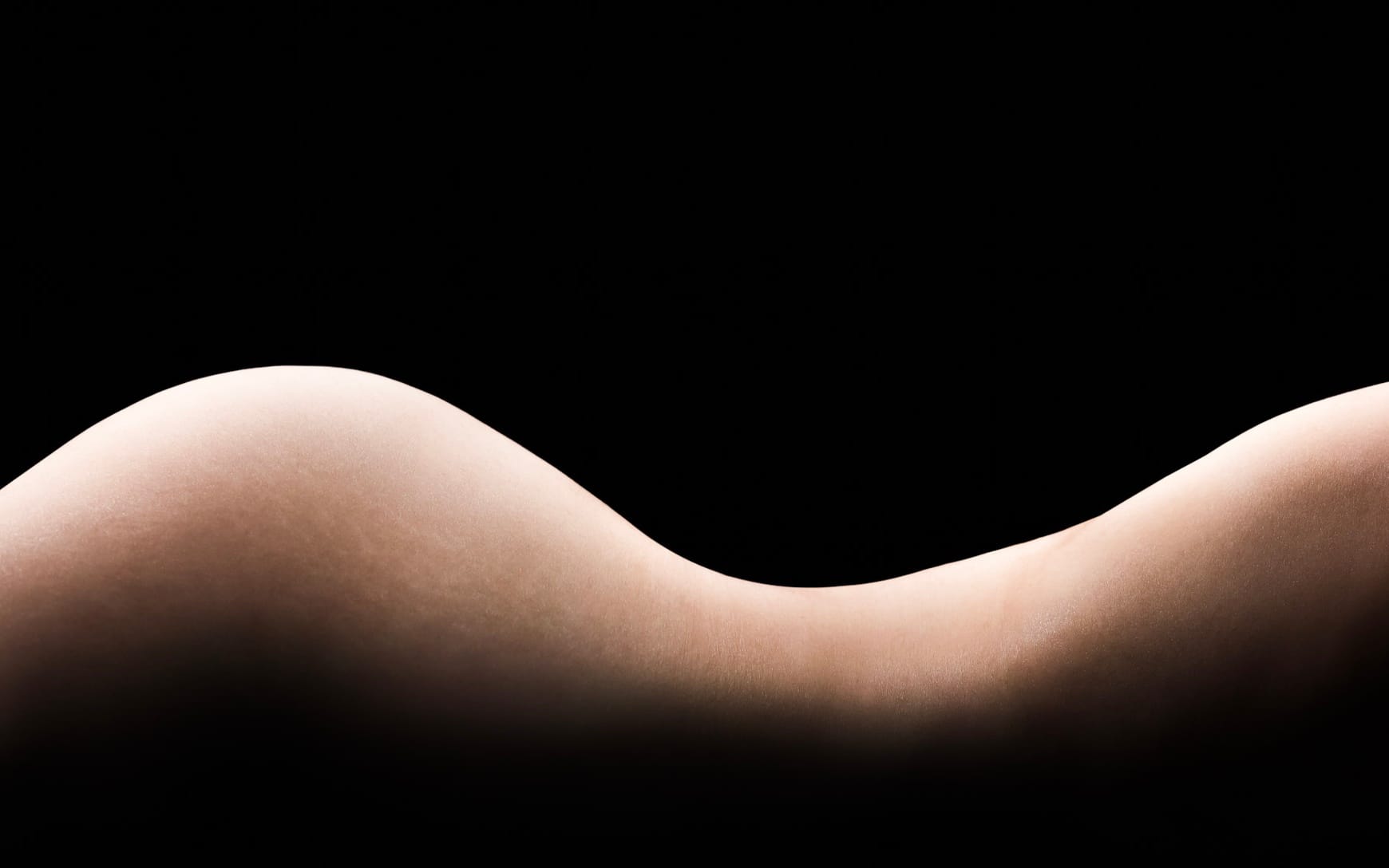 The curve of a back and waist, lit against a dark ground.