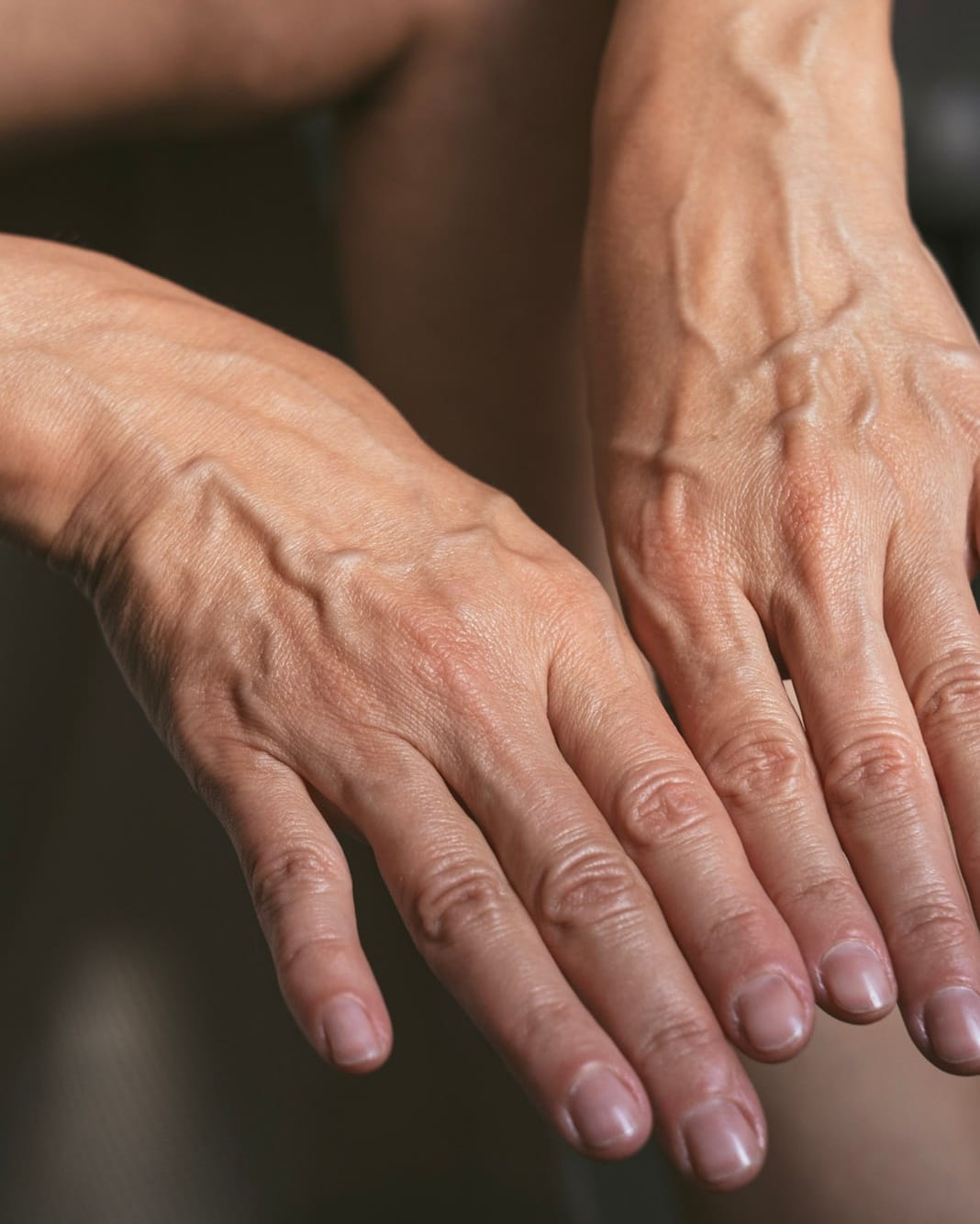 A pair of hands resting one over the other, skin in low side light.