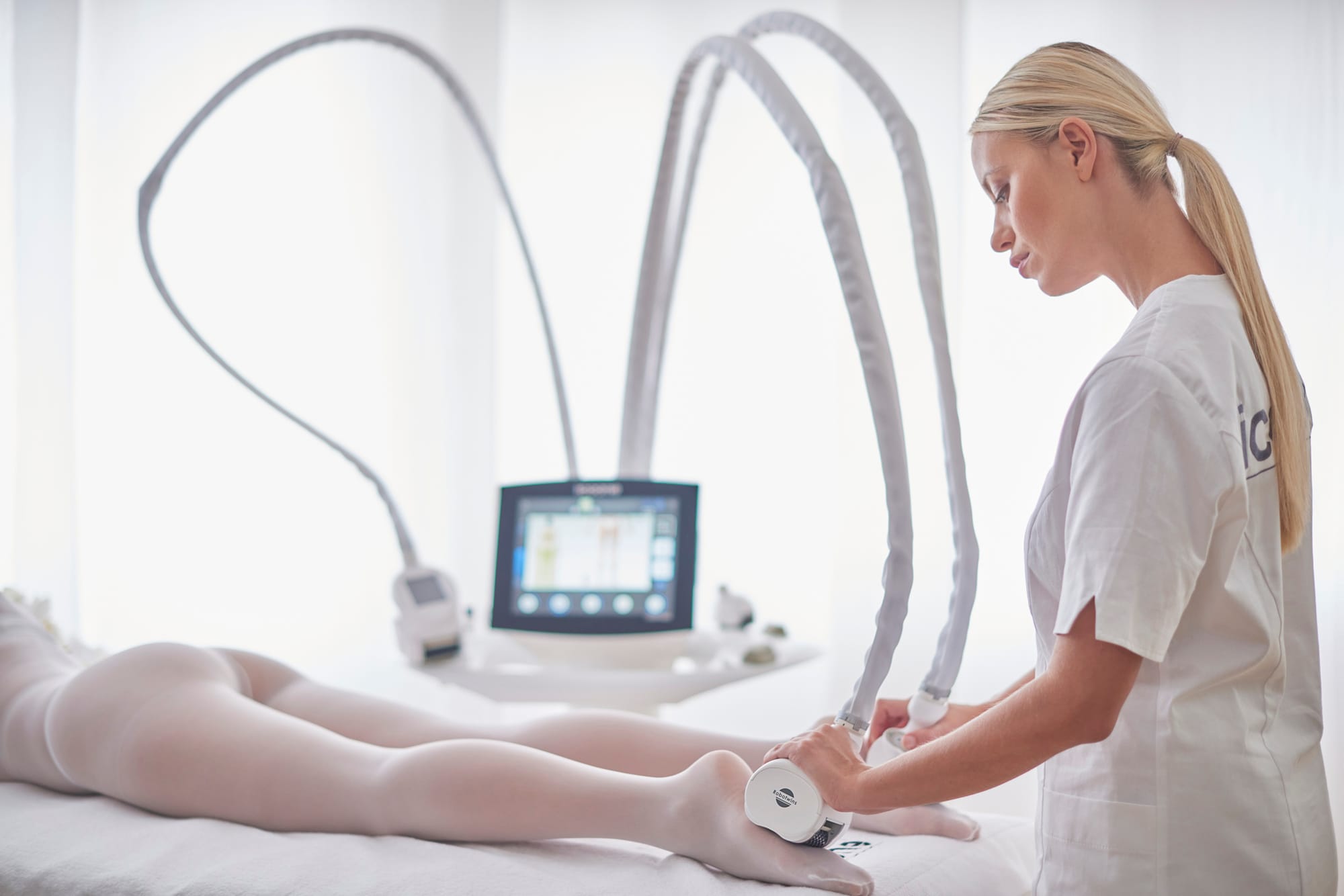 A clinician guiding ICOONE handpieces along a client&rsquo;s leg, the ICOONE console beside the treatment bed.